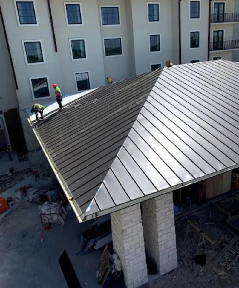 Crew installing standing seam metal roof panels on a commercial project in Sugar Land